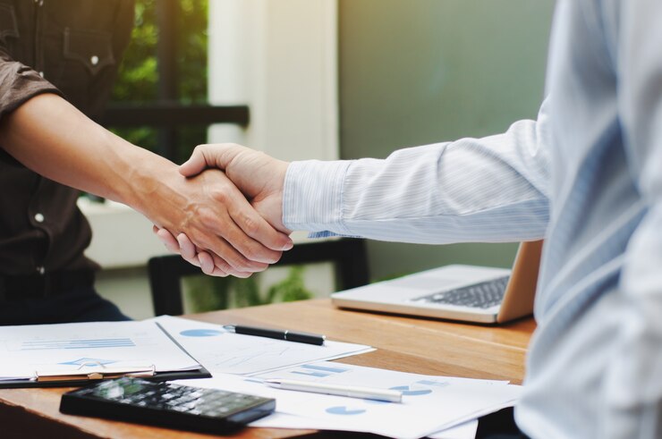 Primer plano de dos ejecutivos de negocios estrechar la mano con los documentos de datos sobre la mesa