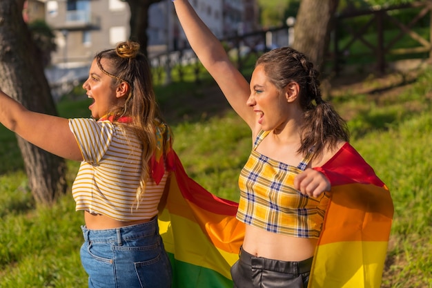 Un primer plano de dos jóvenes mujeres caucásicas abrazando con bandera de orgullo LGBT al aire libre