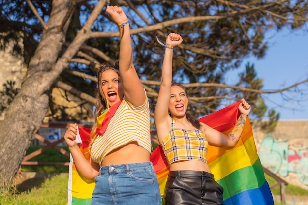 Un primer plano de dos jóvenes mujeres caucásicas sosteniendo la bandera del orgullo LGBT al aire libre