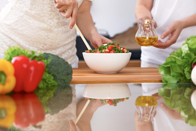 El primer plano de dos mujeres está cocinando en una cocina. Amigos divirtiéndose mientras preparan ensalada fresca.