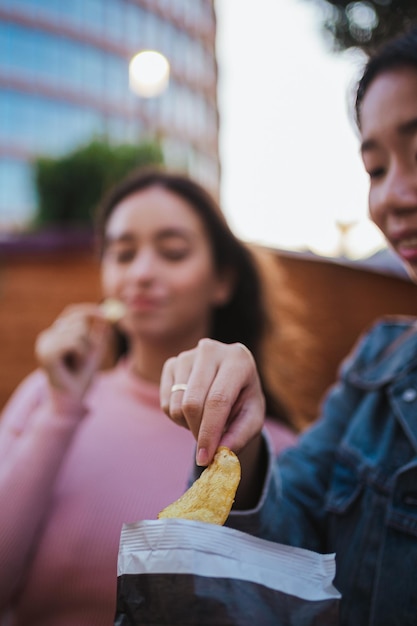 Primer plano de dos mujeres jóvenes comiendo papas fritas de una bolsa mientras se divierten