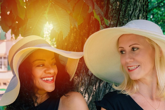 Primer plano de dos mujeres con sombreros de verano mirándose y sonriendo amigable