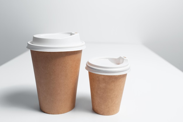 Primer plano de dos vasos de papel para llevar café en la mesa blanca