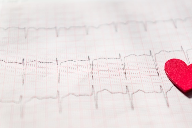 Foto primer plano de un electrocardiograma en forma de papel con corazón de madera roja ecg o ecg de papel fondo textura concepto médico y de atención médica