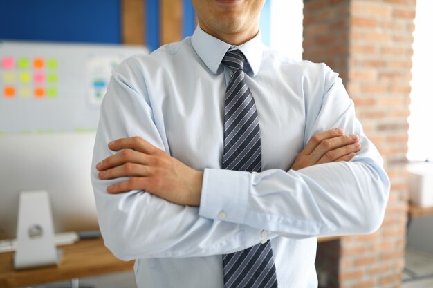 Primer plano de elegante empresario de pie con los brazos cruzados en el gabinete personal. Especialista profesional en disfraces de moda. Hombre exitoso. Diseño de interiores y concepto de negocio.