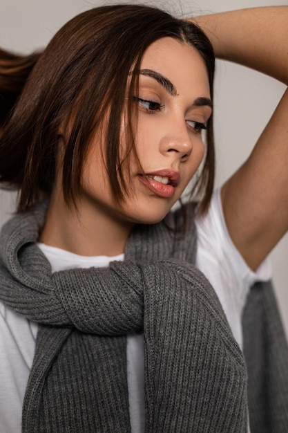 Primer plano elegante retrato de una mujer joven y bonita modelo con una cara linda en ropa de moda con una camiseta blanca y un suéter de punto vintage