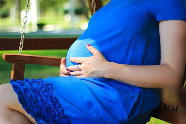 Primer plano de embarazo de niña en vestido azul en un banco