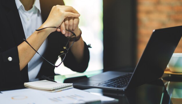 Primer plano de una empresaria sosteniendo anteojos mientras trabaja y mira la computadora portátil en la oficina