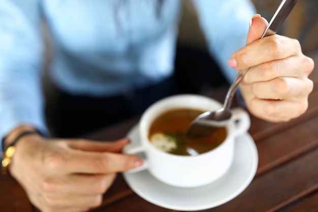 Primer plano de la empresaria sosteniendo la placa y la cuchara. empresaria cenando en la cafetería. Cuenco blanco de pie sobre la mesa de madera. Pausa para el almuerzo en el concepto de trabajo