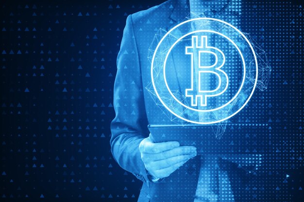 Primer plano de un empresario de píxeles que usa una tableta con un holograma abstracto de bitcoin en un fondo azul Concepto de criptomoneda y finanzas