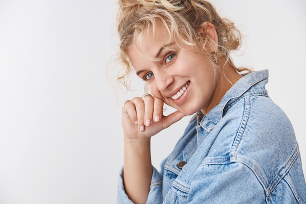 Primer plano encantadora rubia de pelo rizado elegante novia coqueta de ojos azules inclinando la cabeza girando la hermosa cámara sonriendo riendo coqueteando expresando felicidad bienestar encantado, pared blanca