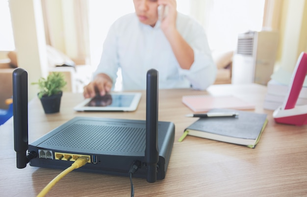 Primer plano de un enrutador inalámbrico y un hombre que usa un teléfono inteligente en la sala de estar en el hogar, equipo para trabajar desde casa,