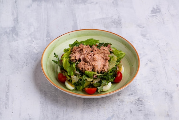 Un primer plano de ensalada de atún en un recipiente aislado sobre un fondo blanco de madera