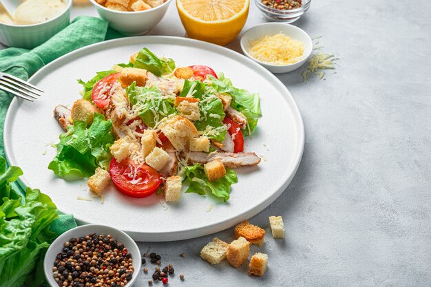 Primer plano de ensalada César en un plato blanco rodeado de ingredientes sobre un fondo gris. El concepto de comida sana.