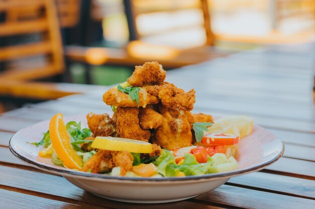 Primer plano de una ensalada con nuggets en un plato blanco sobre una mesa de madera