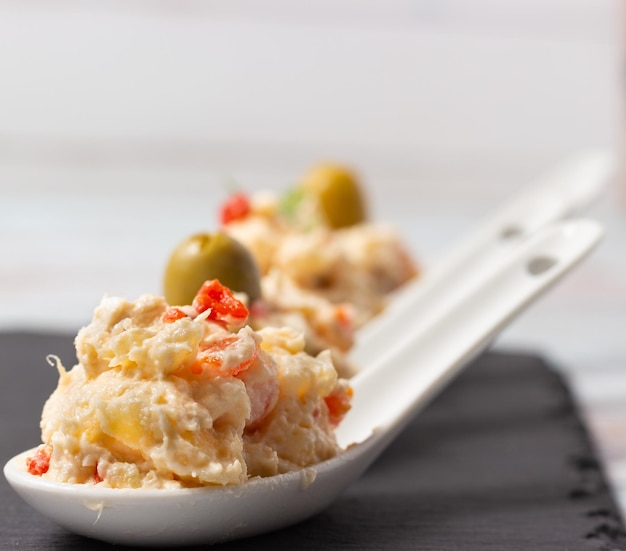 Primer plano de una ensalada rusa Tapa típica española en cucharas de cerámica blanca