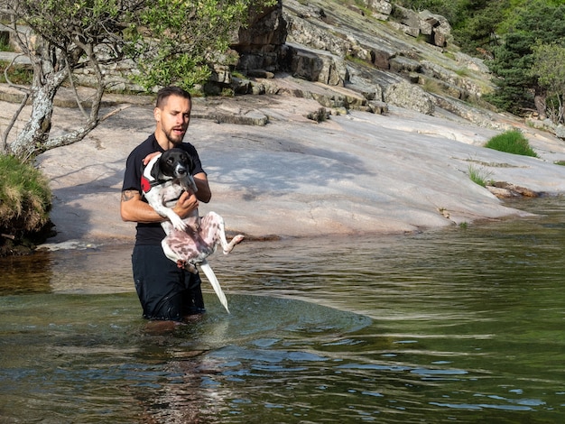 Primer plano de entrenador de perros con cachorro para enseñarle a nadar en un lago. Cachorro blanco y negro aprendiendo a nadar en un lago.