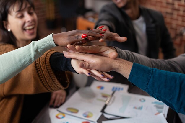 Primer plano de un equipo diverso exitoso sonriendo mientras se pone de la mano celebrando los logros de la empresa durante la reunión de negocios trabajando en la oficina de inicio. Empresarios multiétnicos disfrutando juntos