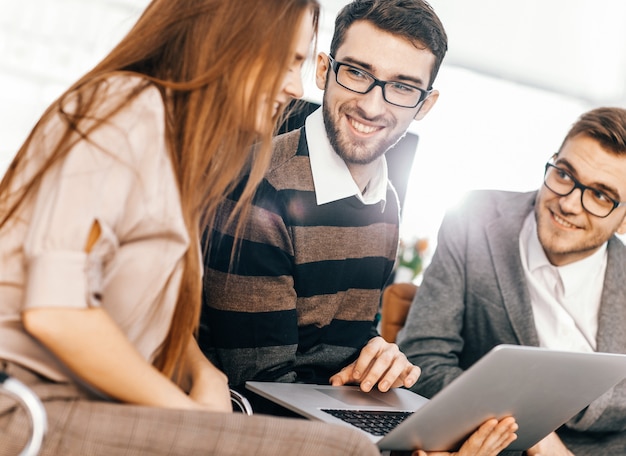 Primer plano de un equipo de negocios amistoso que trabaja en la computadora portátil y que discute asuntos comerciales.