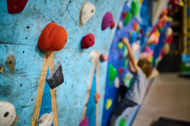 Primer plano de una escalada blanca en una colorida pared de roca interior con un joven escalador borroso en el fondo atmósfera de entrenamiento vibrante y enérgica