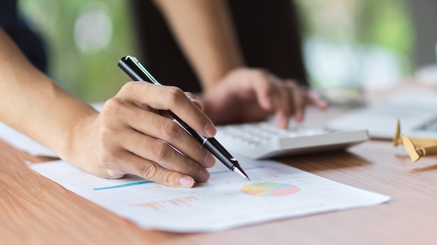 Primer plano de la escritura femenina en el informe financiero mientras calcula en la sala de la oficina