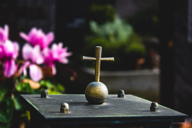 Primer plano de una escultura de símbolo de cruz en un cementerio o cementerio con flores en el fondo