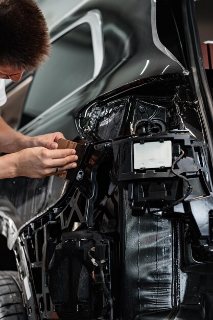 Un primer plano de un especialista en envoltura de automóviles colocando una película protectora en un automóvil en un servicio de detalles