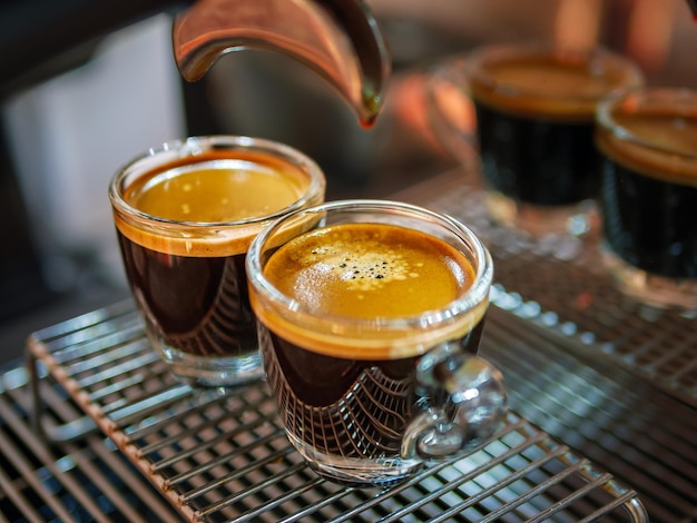 Un primer plano de un espresso disparado con crema de café y la preparación de dos vasos de espresso disparados en una cafetería