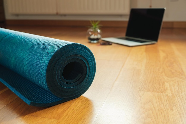 Primer plano de una estera de yoga y una computadora portátil preparada para una clase de yoga en línea en casa