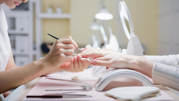 Primer plano de una esteticista pintando las uñas de una mujer con un pincel en un salón de uñas