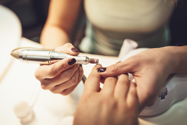 Primer plano de una esteticista puliendo las uñas de los clientes femeninos con lima de uñas en el salón de belleza.