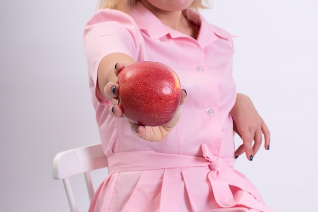 Primer plano de una esteticista en un uniforme rosa sosteniendo una gran manzana roja inyecciones de Botox