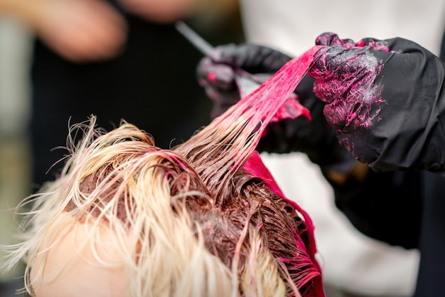 Primer plano de estilista de cabello teñido de mujer con tinte rosa en peluquería