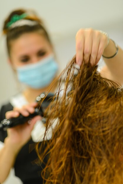 Foto un primer plano de una estilista trabajando con una pelirroja y usando una máscara facial: el concepto de la nueva normalidad