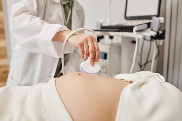 Primer plano del examen de ultrasonido de la mujer embarazada con enfoque en el médico que sostiene el transductor al espacio de la copia del vientre