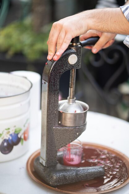 Primer plano del exprimidor mecánico de hierro exprimiendo jugo de granada o tomate en un vaso de precipitados