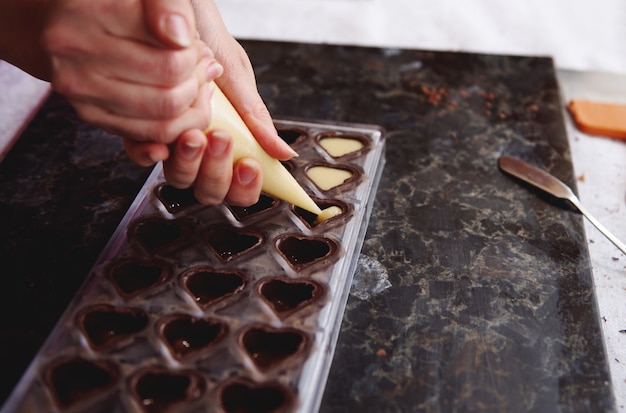 Primer plano de exprimir el relleno de crema de caramelo salado de la bolsa de confitería en moldes de caramelo para preparar pralinés de chocolate artesanales