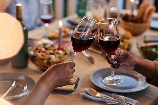 Primer plano de la familia tintineando copas de vino en la mesa de la cena al aire libre ambiente acogedor por la noche