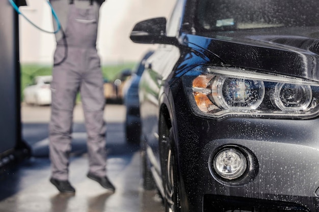 Un primer plano de los faros de los automóviles con un hombre de servicio en la estación de lavado de automóviles