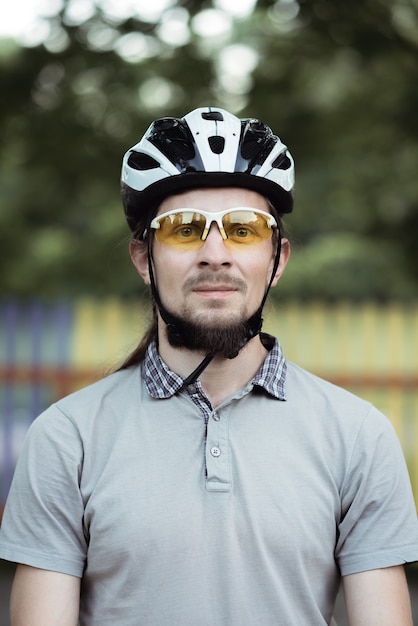 Primer plano de feliz atractivo joven con barba con casco protector y gafas de sol amarillas mirando al frente