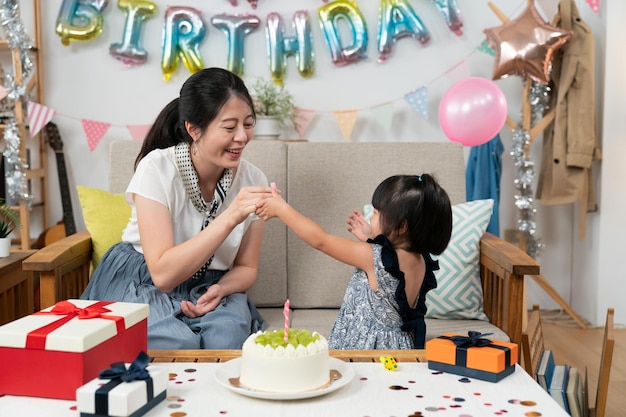 primer plano de la feliz madre asiática y la niña divirtiéndose con silbatos de fiesta en la fiesta de cumpleaños en casa