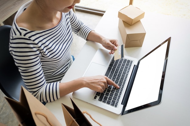 Primer plano de feliz mujer joven celebración de tarjeta de crédito de información de la tarjeta de entrada mientras y utilizando equipo portátil en casa. Concepto de compras en línea.