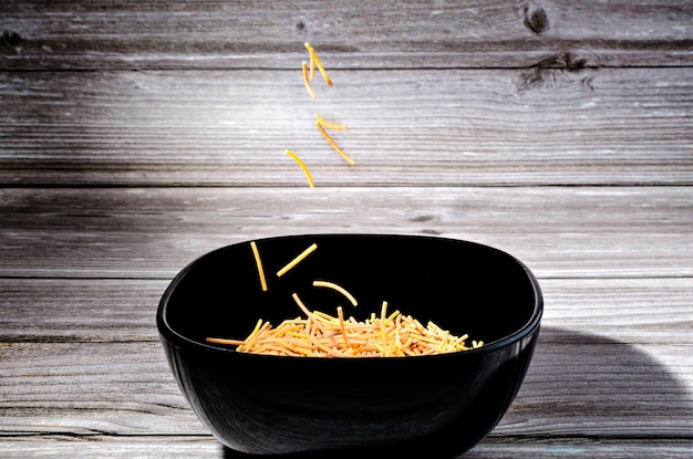 Primer plano de fideos de polifosfato cocidos en un cuenco de cerámica negra sobre una mesa de madera.