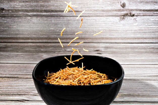 Foto primer plano de fideos de polifosfato cocidos que caen en un cuenco de cerámica sobre una mesa de madera.