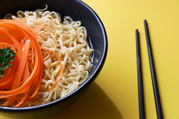 primer plano de fideos ramen vegetarianos con palillos sobre fondo amarillo