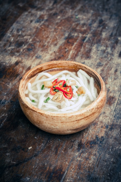 Primer plano de fideos udon en tazón de madera sobre suelo de madera