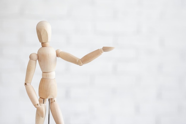 Primer plano de la figura humana de madera apuntando a algo sobre fondo de pared de ladrillo blanco