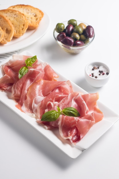 Primer plano de finas lonchas de prosciutto con aceitunas mixtas