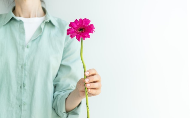 Foto primer plano de una flor en la mano de una niña de pie sobre un fondo claro lugar para el texto