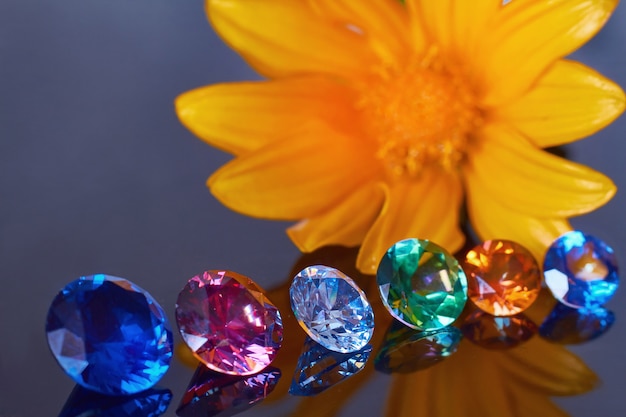 Primer plano de flor de naranja y varios cristales elegantes en una superficie de espejo negro profundo, brillan y brillan